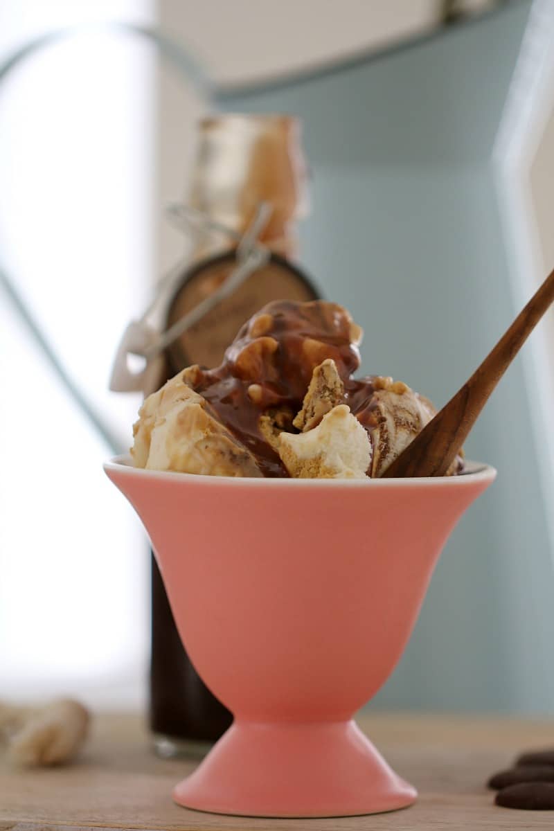 A pink parfait cup with a small wooden spoon, piled with ice cream and drizzled with Baileys Fudge Sauce