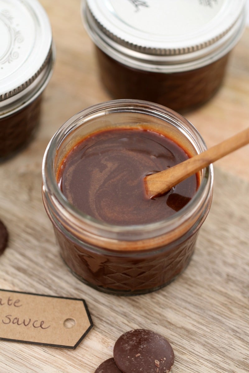 A glass jar filled with chocolate fudge sauce, with a handwritten label beside it.