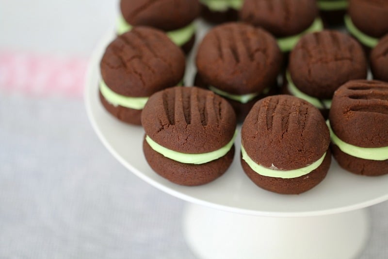 A white cake stand with chocolate biscuits sandwiched together with mint icing 