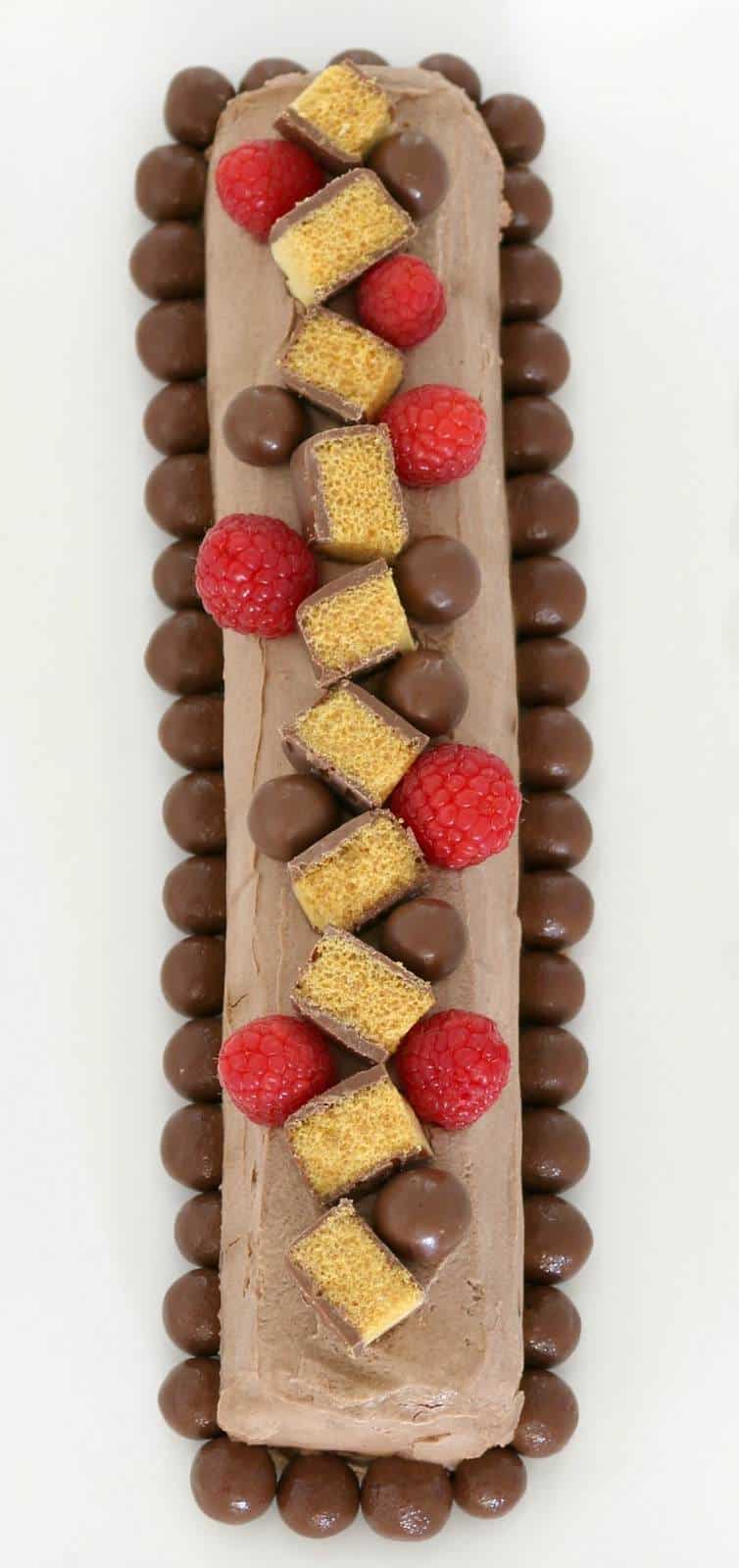 An overhead shot of a chocolate log cake topped with chopped chocolate honeycomb, raspberries and Maltesers