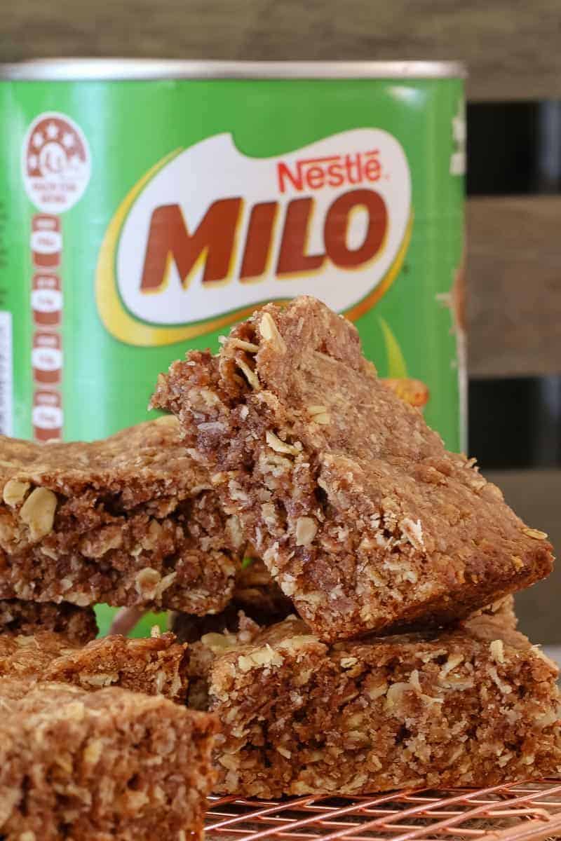 A stack of crunchy chocolate & oat slices in front of a tin of Milo