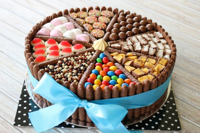 A blue ribbon tied in a bow around a chocolate cake decorated with lollies and chocolates.