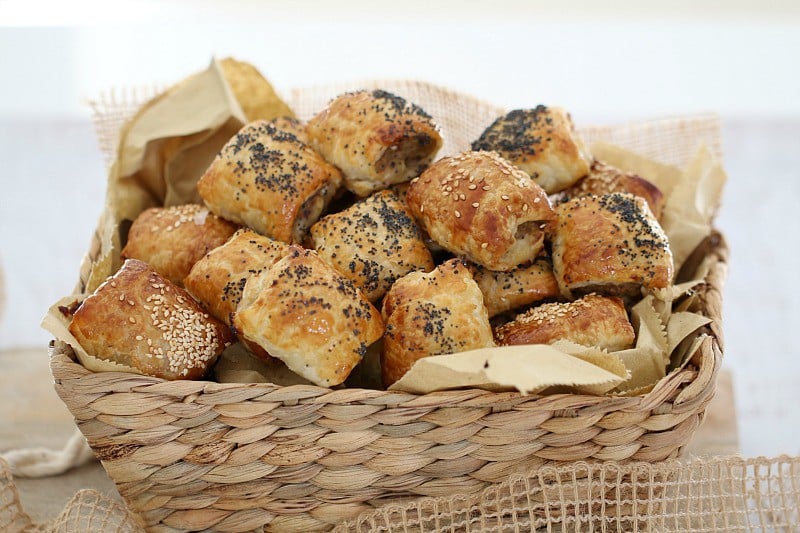 A basket piled with mini sausage rolls baked golden and sprinkled with seeds