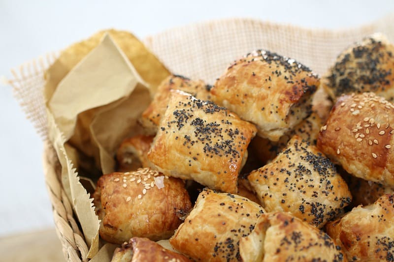 A close up of a pile of mini sausage rolls sprinkled with poppy seeds and sesame seeds