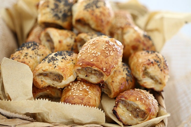 Sesame seeds and poppy seeds on top of mini sausage rolls baked golden and piled together in a basket