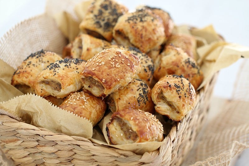 Mini sausage rolls piled in a basket, some sprinkled with poppy seeds, some with sesame seeds