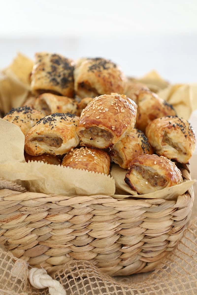 A basket filled with mini sausage rolls baked golden and sprinkled with seeds