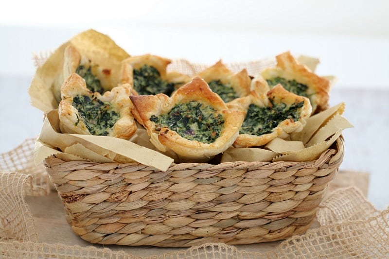 A basket piled with golden pastry spinach and ricotta tarts