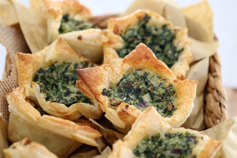 A close up of spinach and ricotta tarts in golden puff pastry squares