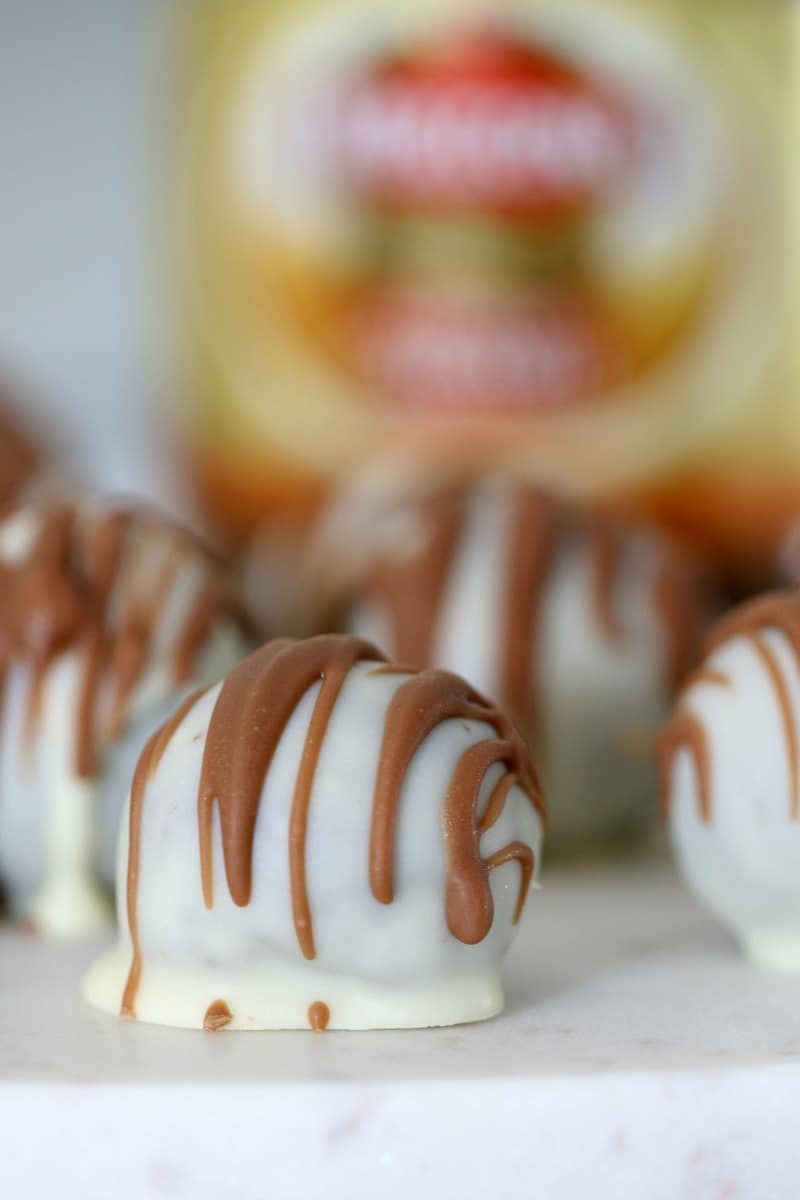 A close up of white chocolate coated choc-mocha cheesecake balls, drizzled with milk chocolate