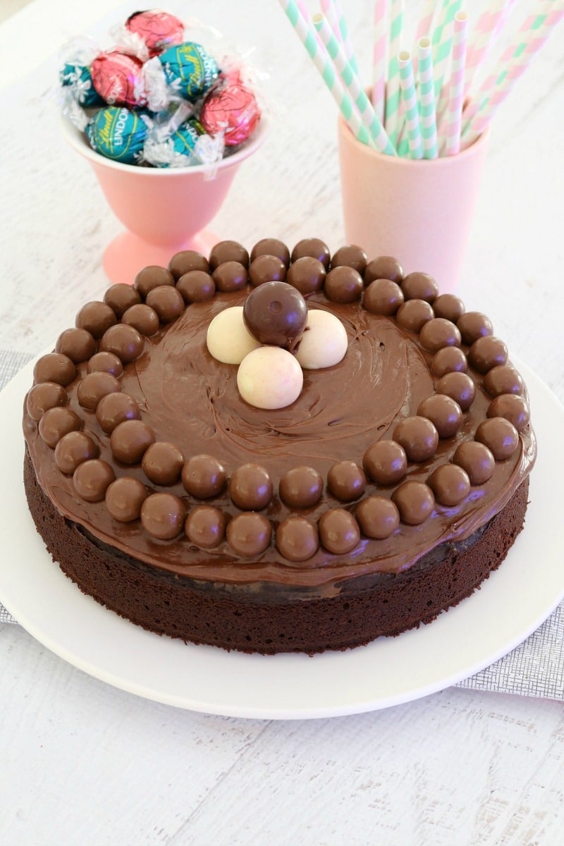A white plate with a round chocolate cake decorated with Maltesers and Lindt balls