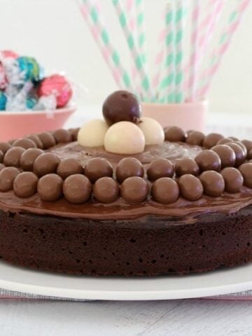 A large round chocolate cake topped with Maltesers and Lindt balls on chocolate ganache frosting