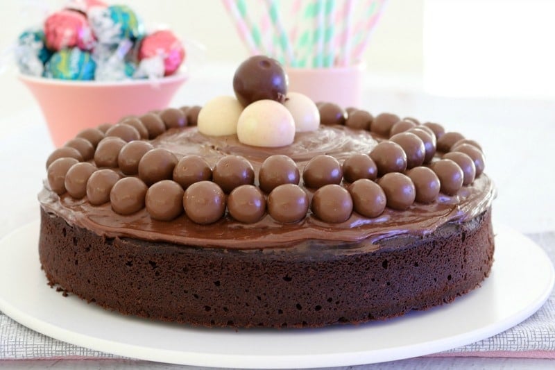 A chocolate cake on a plate with chocolate ganache, Maltesers and Lindt balls on top