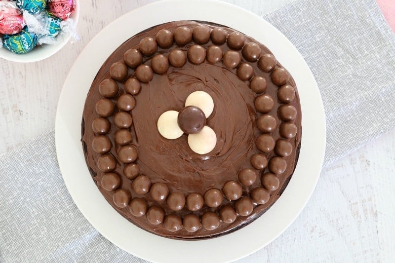 Looking down on two circles of Maltesers around the edge of a chocolate cake, with 4 Lindt balls in the centre