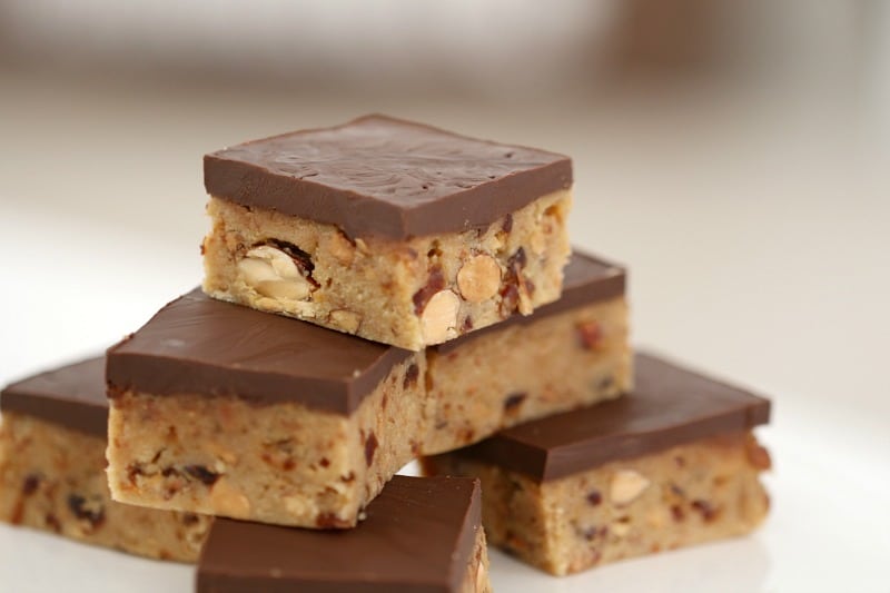 A close up of squares of a date and almond slice, topped with chocolate and stacked in a pile