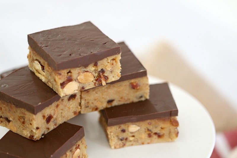 Squares of a slice with a layer of chocolate on top and dates and almonds inside stacked on a plate
