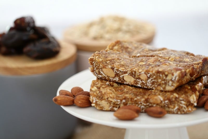Slices of date and oat slice and raw almonds on a cake stand