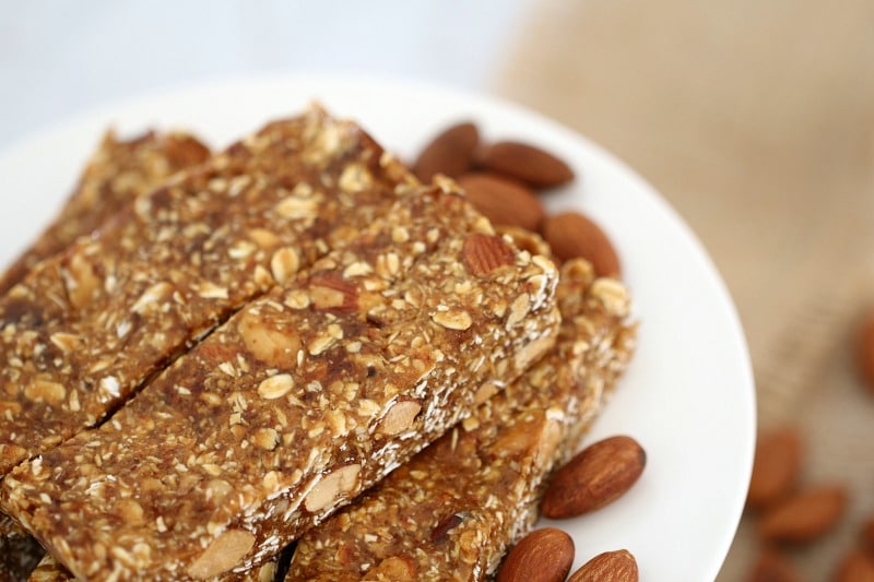 A close up of pieces of slice filled with dates, oats and almonds, and some natural almonds on the plate