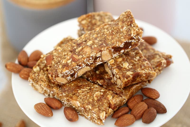 Pieces of date and oat slice in a pile and some natural almonds on a white cake stand