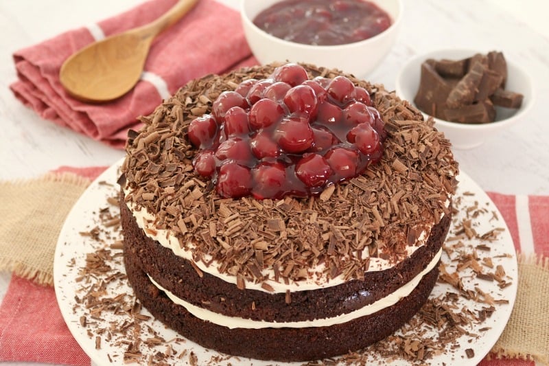 A layered black forest chocolate cake topped with whipped cream, grated chocolate and a pile of morello cherries on the top