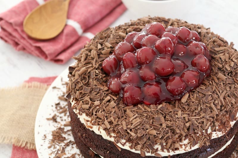 Looking down on a round layered chocolate cake topped with whipped cream, grated chocolate and a pile of morello cherries on top