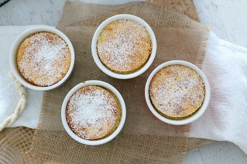 An overhead shot of four small ramekins filled with baked lemon pudding and dusted with icing sugar