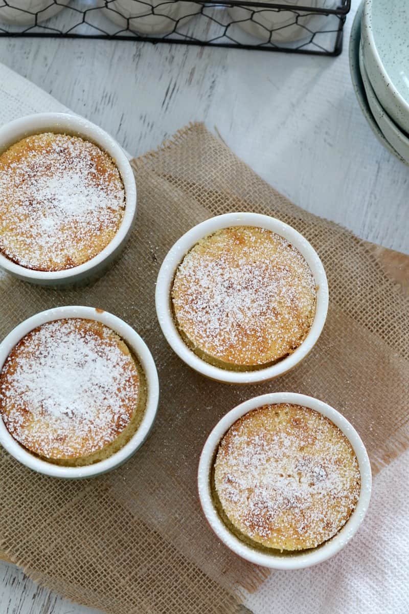 Looking down on four small ramekins filled with baked lemon puddings dusted with icing sugar
