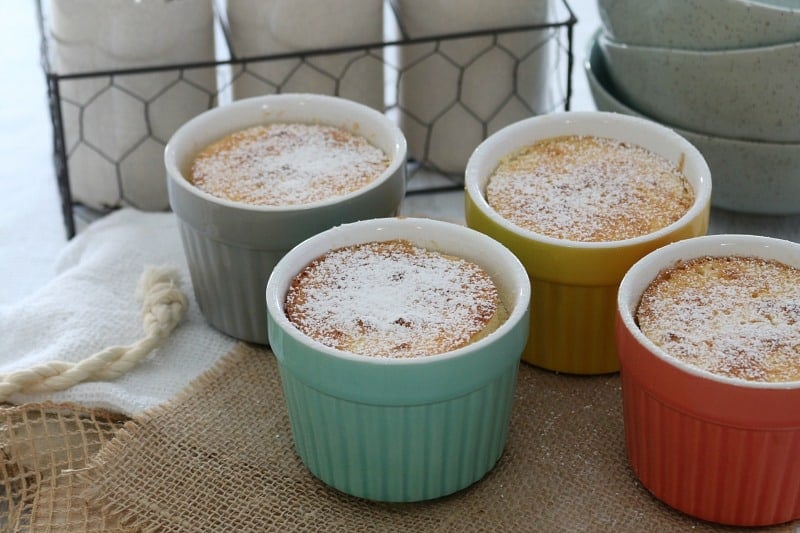 icing sugar dusted over baked lemon pudding in small coloured ramekins on a bench