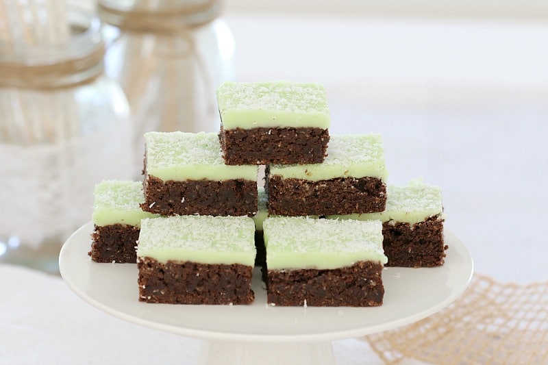 A stack of chocolate slice pieces topped with a mint icing on a white plate