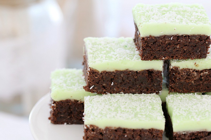 Pieces of chocolate slice with a mint icing and sprinkled with coconut on top, stacked and served on a plate