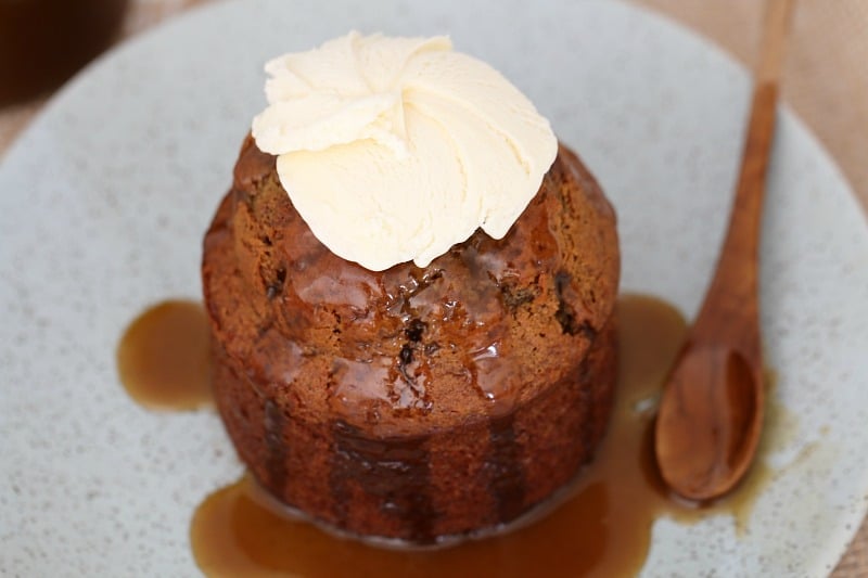 An overhead shot of an individual sticky date pudding served with whipped cream and caramel sauce