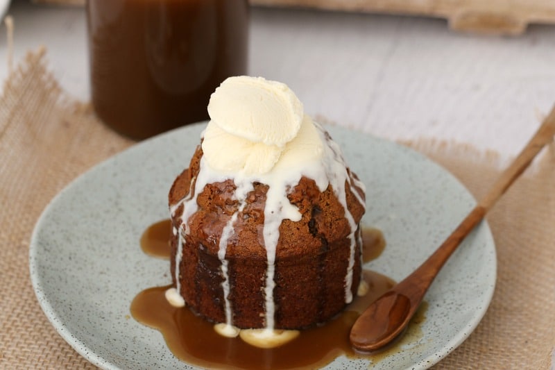Ice cream melting over an individual sticky date pudding with caramel sauce drizzled over.