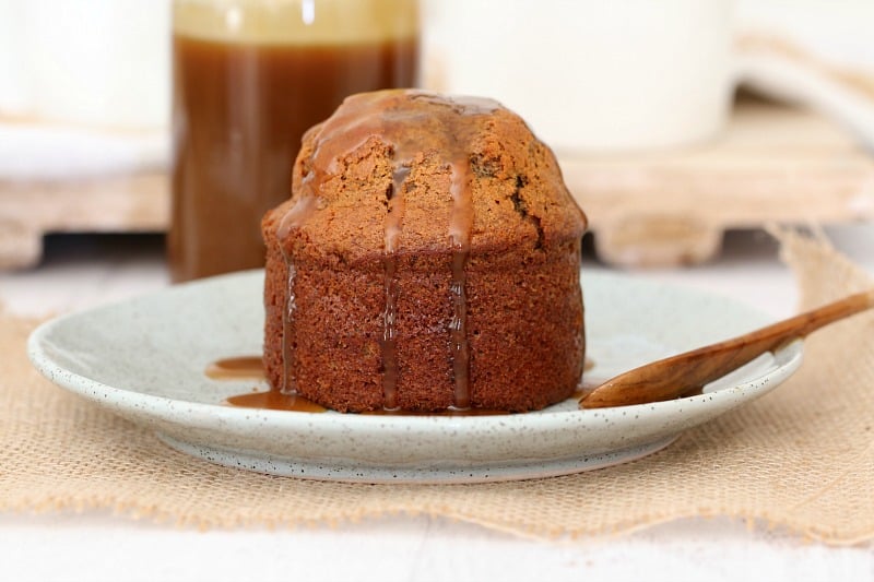 A side view of a small sticky date pudding with caramel sauce drizzled over it.