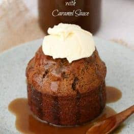 An individual sticky date pudding drizzled with caramel sauce and topped with whipped cream on a plate