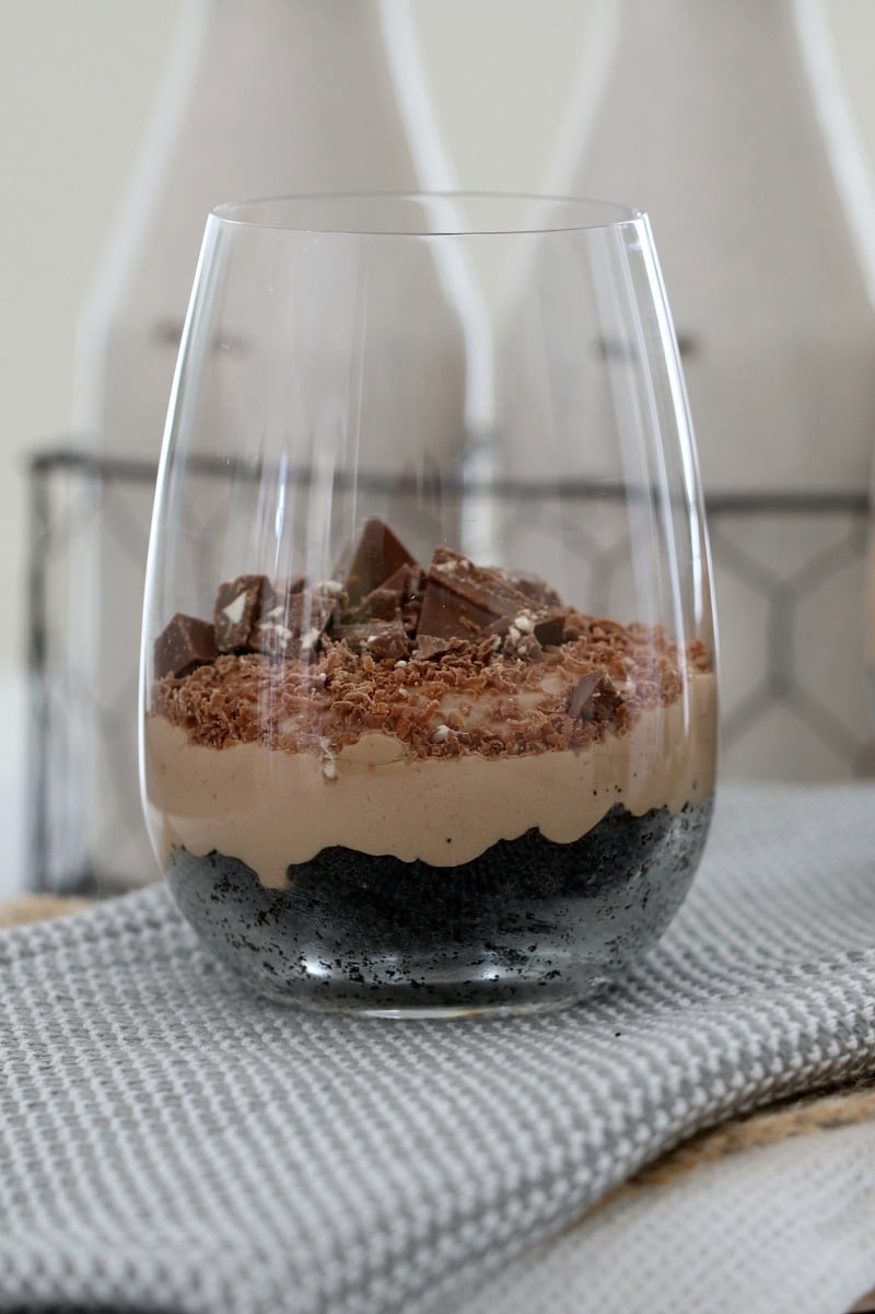 A stemless wine glass filled with chocolate cheesecake and chuncks of Toblerone chocolate on top.