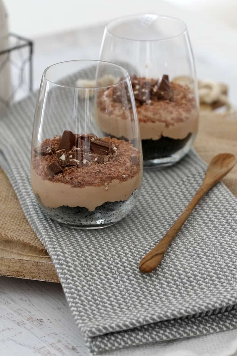 Two mini no-bake Toblerone cheesecakes in glasses next to a wooden spoon