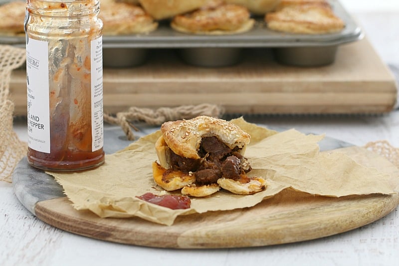 Chunky meat filling inside a split open pastry and meat pie, served with a dollop of tomato sauce on a wooden board