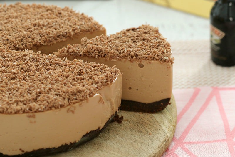 A chocolate cheesecake on a wooden board with one slice cut.