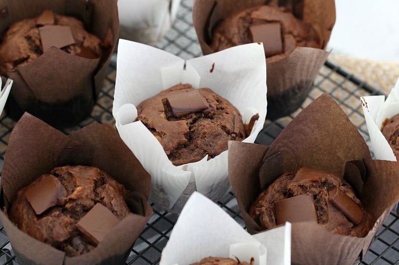 Chocolate muffins with chunks of chocolate on top, and wrapped in baking paper sitting on a wire rack
