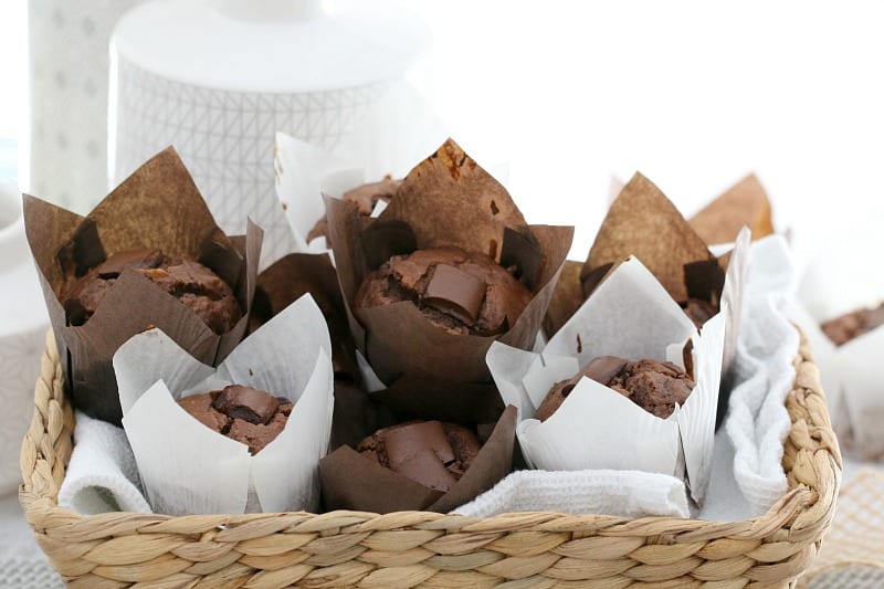 A basket filled with wrapped chocolate muffins with pieces of chocolate on top