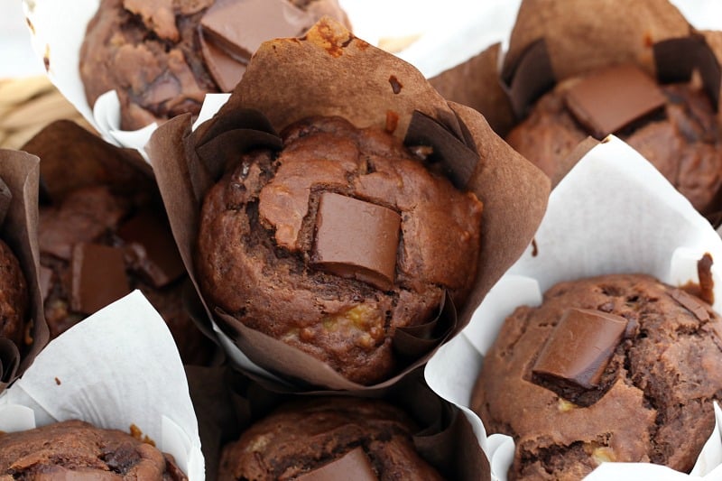A close up of wrapped muffins with chocolate chunks on top