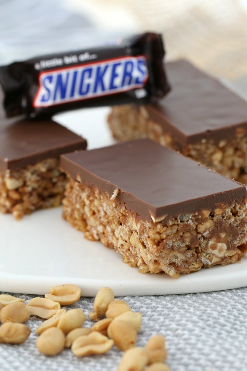 A close up of pieces of Snicker Slice showing a filling made with rice bubbles, peanuts and Snickers Bars, topped with milk chocolate, and showing a mini Snickers Bar 