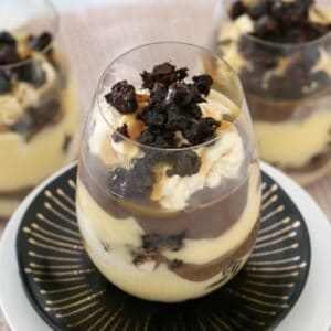 A glass of decorated trifle on a black plate in front of more trifle filled glasses.