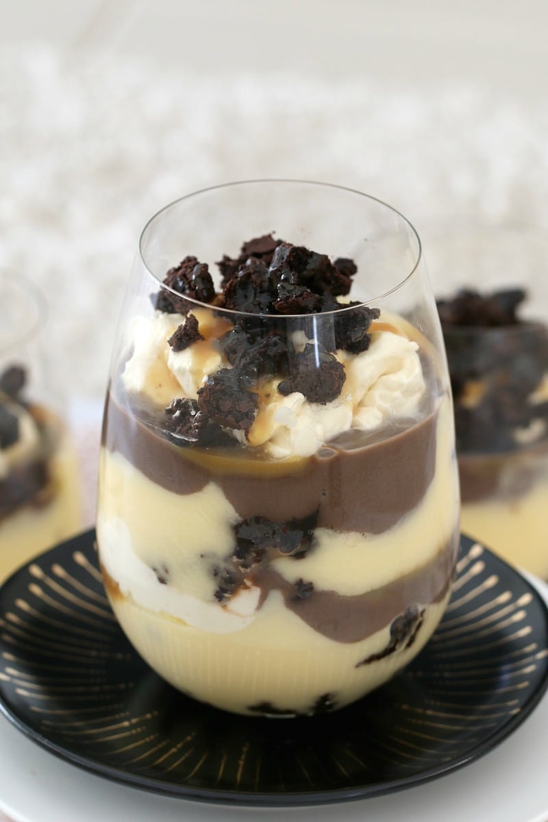 A glass cup filled with brownie, custard, Baileys, cream and caramel sauce in layers.