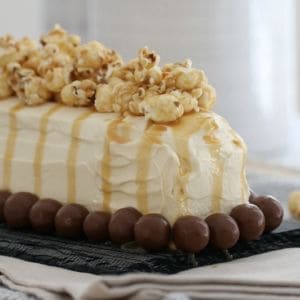 A log cake covered in cream and drizzled with caramel sauce, decorated with Malteser balls around the edge and salted caramel popcorn on top