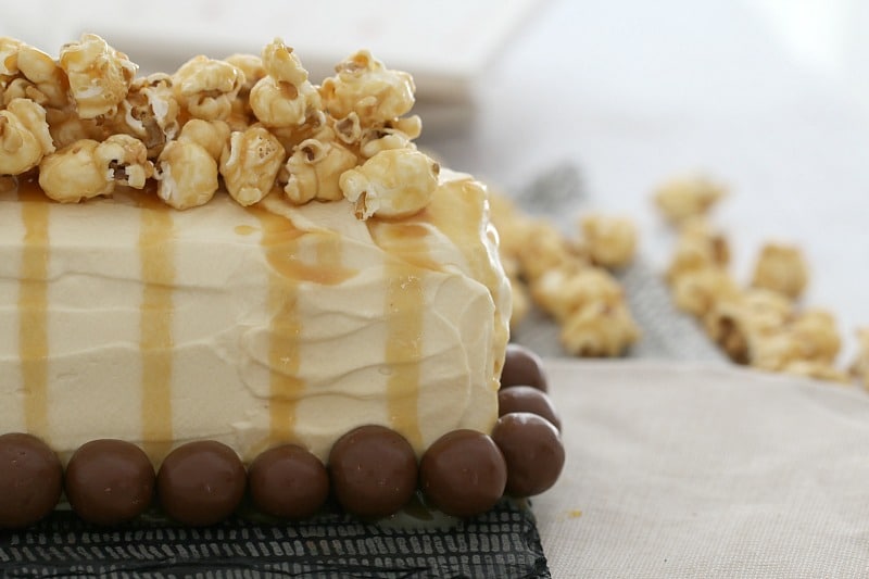 Popcorn drizzled with caramel sauce on top of a cream log cake with Malteser balls around the base