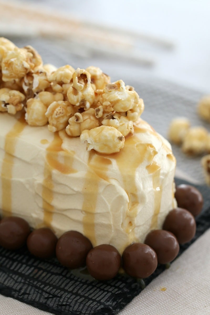 A close up of popcorn drizzled with caramel sauce on top of a cream covered log cake, and Maltesers around the base