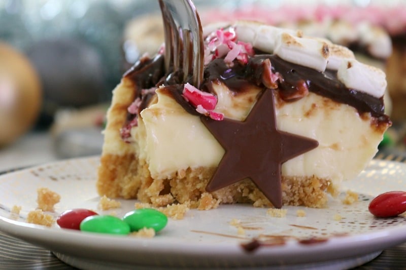 A slice of S'mores Christmas Cheesecake on a plate with a fork taking a bite