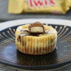 A mini cheesecake with a piece of Twix bar on top, served on a black plate