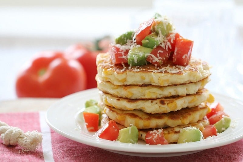 A stack of corn fritters served with a chunky tomato and avocado salsa on top